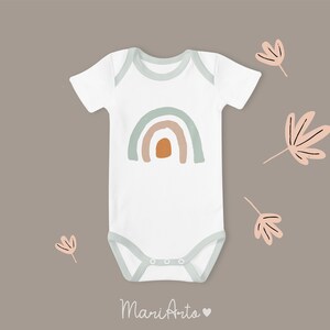 K&ouml;nnte beinhalten: Wei&szlig;er Baby-Strampler mit einem Regenbogen-Design in Gr&uuml;n-, Orange- und Braunt&ouml;nen. Der Strampler hat einen Druckknopfverschluss am Boden und ist mit kleinen wei&szlig;en Punkten verziert.