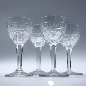 May include: Set of four clear glass stemmed drinking glasses with a cut glass design. The glasses are arranged in a row, with the front glass slightly overlapping the others.