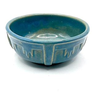 May include: A small, light blue ceramic bowl with a decorative design around the rim and sides. The bowl has a slightly rounded bottom.