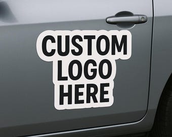 May include: A white car magnet with the words "CUSTOM LOGO HERE" in bold black letters. The magnet is affixed to the side of a gray car, near the door handle.