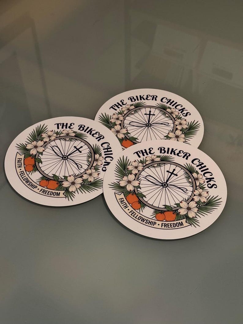 Peut inclure: Trois autocollants circulaires blancs pr&eacute;sentant un dessin au trait noir d'une roue de v&eacute;lo centr&eacute;e avec une croix. Le motif inclut des fleurs blanches, des feuilles vertes et des fruits orange. Le texte indique THE BIKER CHICKS et FAITH FELLOWSHIP FREEDOM.