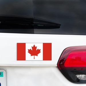 May include: A white car with a Canadian flag sticker on the back. The flag is red and white with a red maple leaf in the center.