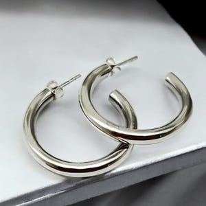 May include: A pair of silver hoop earrings. The hoops are thick and have a smooth, polished finish.