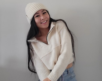 May include: A woman wearing a white knitted zip-up sweater and a white beanie. The text "Billie Zip & Beanie Knitting Pattern Bundle" is written above her head.