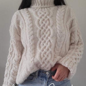 Peut inclure: Un pull en tricot blanc à torsades avec un col roulé. Le pull a un texte superposé "Maurizio Sweater Knitting Pattern".