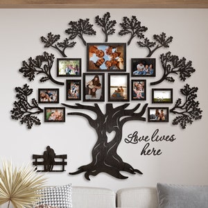 Könnte beinhalten: Schwarze Metall-Wandkunst in Form eines Baumes mit mehreren Fotorahmen, die einen Familienstammbaum darstellen. Das Baumdesign enthält ein herzförmiges Element und den Schriftzug "Love lives here". An einer weißen Wand über einem weißen Sofa.