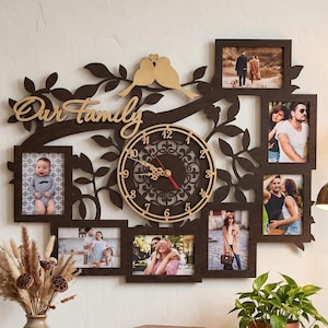 Può includere: Un orologio da parete in legno marrone scuro con un design a rami d'albero, la scritta Our Family, sei cornici rettangolari e un quadrante centrale circolare con numeri e lancette color oro, montato su una parete chiara.