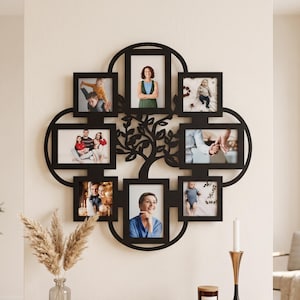 May include: A black wall-mounted photo frame featuring a central tree silhouette design with seven rectangular openings for photographs. The frame is arranged in a circular pattern with a tree motif integrated into the center, holding various family photos.