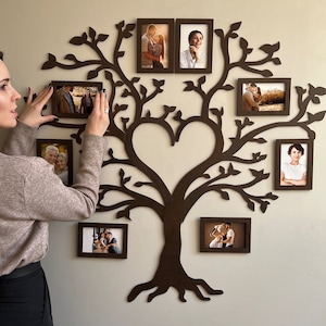 Puede incluir: Decoración de pared de árbol genealógico de madera marrón oscuro con múltiples marcos de fotos. El diseño del árbol presenta un centro en forma de corazón y ramas que sostienen marcos rectangulares con fotografías. Decoración mural.