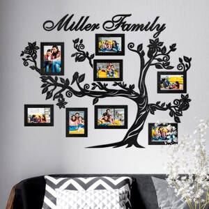 May include: Black wooden family tree wall decor with eight black picture frames, each holding a family photo. The tree has a whimsical design with leaves and flowers. The text "Miller Family" is at the top of the tree.