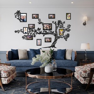 May include: A black metal family tree wall decor with multiple photo frames. The frames are arranged in a tree shape and feature photos of different people. The decor is mounted on a white wall in a living room setting.
