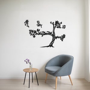 May include: Black metal wall art featuring a stylized tree with intricate branches and leaves. The tree is mounted on a white wall, with a gray armchair and a small wooden table with a vase of purple flowers in front of it.