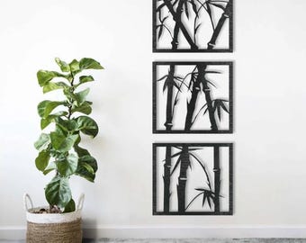 May include: Three square, black bamboo wall art panels. Each panel features a silhouette of bamboo stalks and leaves against a white background. The panels are mounted on a white wall above a gray floor. A potted plant is in the foreground.
