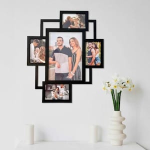 May include: A black multi-photo frame with various family photos. The frame has a unique geometric design and holds several pictures of different sizes. A white vase with white flowers and two white candles are in the foreground.