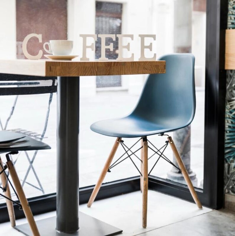 May include: A modern cafe scene featuring a wooden table with the word "COFFEE" spelled out in white letters. A blue plastic chair with wooden legs and a white teacup on a saucer are also visible.