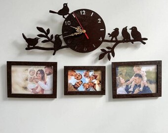 May include: A decorative wall clock with a dark brown circular face and black numbers, surrounded by a branch with birds. Below are three framed family photos with dark brown frames. The clock has a red second hand.