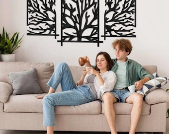 May include: Three-piece black metal wall art featuring tree branch designs within rectangular frames. The artwork is mounted on a white wall above a beige sofa. A couple is relaxing on the sofa.