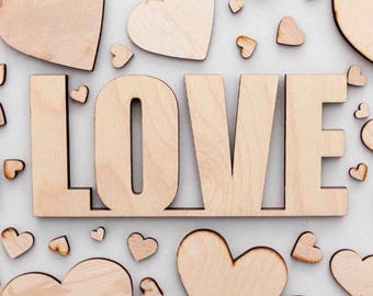 May include: Wooden letters spelling "LOVE" surrounded by various sizes of wooden hearts. The letters and hearts are light brown and arranged on a light gray background. A charming and romantic theme.