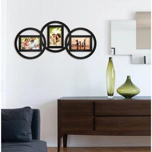 May include: A black, circular wall-mounted photo frame with three connected frames. Each frame holds a photograph. The frames are arranged in a horizontal line, with the center frame slightly overlapping the other two. The photos depict family portraits.