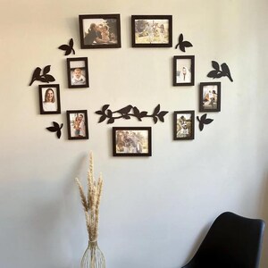 Peut inclure: Une composition murale de cadres photo noirs disposés en cercle, agrémentée de découpes décoratives d'oiseaux et de feuilles noires. Les cadres contiennent des photos de famille, créant une décoration murale personnalisée. L'ensemble est fixé sur un mur de couleur neutre.