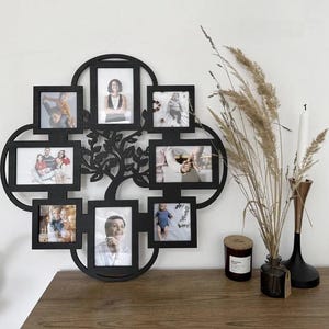 May include: A black, tree-shaped photo frame with eight picture openings. The frame is made of wood and has a decorative tree design in the center. The frame is displayed on a wooden surface with a candle and vase.