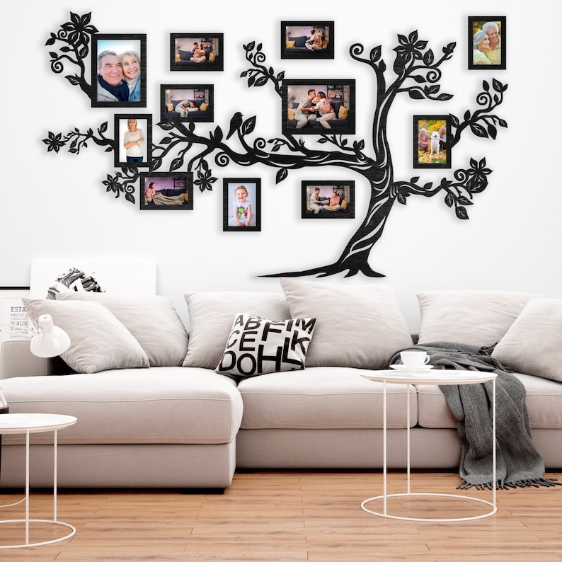 May include: A black metal tree wall decor with multiple black picture frames. The tree has a whimsical design with leaves and birds. The frames are empty and ready for photos. The tree is mounted on a white wall above a white couch with a black and white patterned pillow.