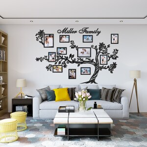 May include: A black silhouette of a tree with branches extending out to hold family photos in black frames. The tree is mounted on a white wall with the text "Miller Family" above it. A white couch with yellow and black pillows is in front of the tree.