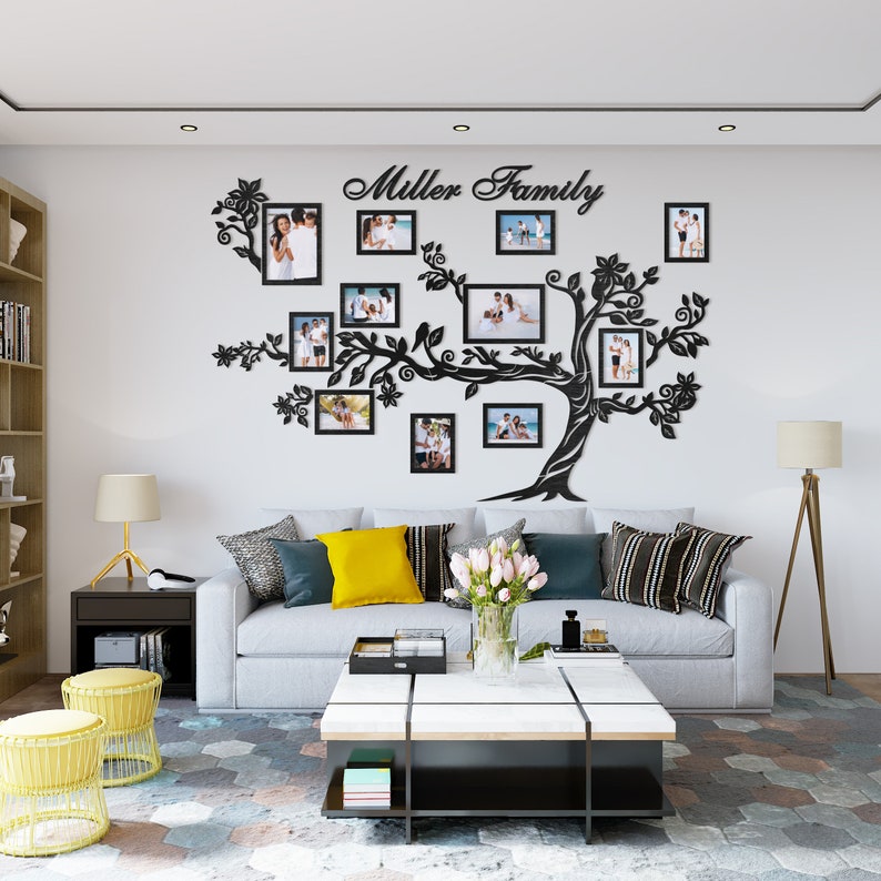 May include: A black silhouette of a tree with branches extending out to hold family photos in black frames. The tree is mounted on a white wall with the text "Miller Family" above it. A white couch with yellow and black pillows is in front of the tree.