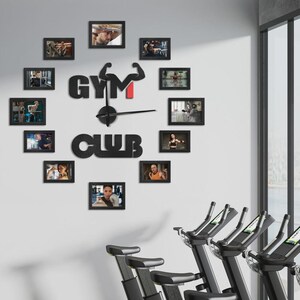 May include: A black wall clock with the words "GYM CLUB" and a weightlifting arm design. The clock is surrounded by framed photos of people working out. The clock is mounted on a white wall, with exercise equipment in the foreground.
