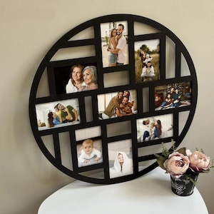 May include: A black, round multi-photo frame with various family photos. The frame has a geometric design with rectangular and square openings. A small black and floral pot with pink flowers sits on a white surface.