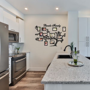 May include: A black metal family tree wall decor with the text "Bacula Family" and 16 photo frames. The decor is mounted on a white wall in a kitchen setting.