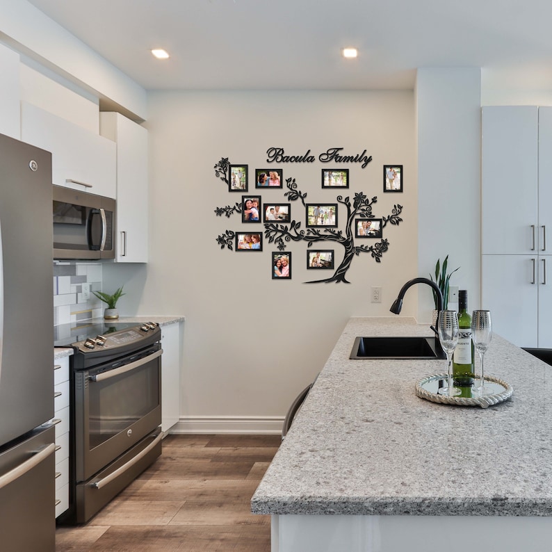 May include: A black metal family tree wall decor with the text "Bacula Family" and 16 photo frames. The decor is mounted on a white wall in a kitchen setting.