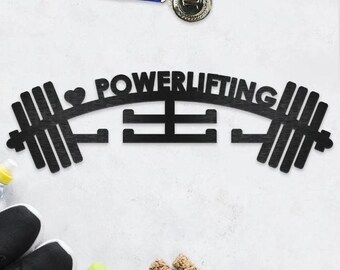 May include: Black wooden barbell-shaped wall art with the word "POWERLIFTING" and a heart symbol. A gold medal with a blue and yellow ribbon is at the top. Other fitness items, including sneakers, dumbbells, and a measuring tape, are at the bottom.