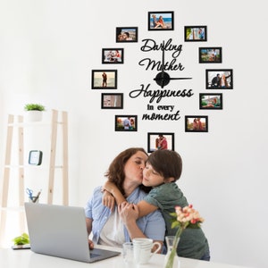 Op de afbeelding: Een zwarte fotoklok met een witte achtergrond. De klok heeft een zwarte lijst en zwarte wijzers. De klok is versierd met foto's van een gezin. De klok heeft de tekst "Darling Mother Happiness in every moment" erop.