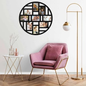 Pode incluir: Uma moldura de fotos múltipla preta e circular com um design geométrico, montada em uma parede branca. A moldura contém várias fotos de família. Uma poltrona rosa com pernas douradas e uma luminária de chão estão em primeiro plano.