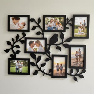 May include: A black metal wall-mounted photo display featuring eight picture frames of various sizes. The frames are arranged in a decorative pattern with a bird and leaf design. The frames hold family photos.