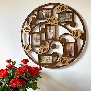 May include: A circular wooden photo frame in dark brown, with spaces for several pictures and lotus flower decorations. The frame is mounted on a white wall. A bouquet of red roses is in the foreground.