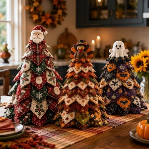 Op de afbeelding: Drie decoratieve stoffen bomen op een tafel. De linkerboom heeft een kerstman-top met rode, groene en witte patronen. De middelste boom heeft een kalkoen-top met herfstbladeren en de rechterboom heeft een spookje als top met Halloween-motieven.
