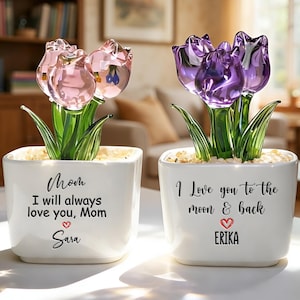 May include: Two decorative glass tulip flower arrangements in white square pots. One has pink tulips, the other purple. Each pot has a message and a name: "Mom, I will always love you, Mom, Sara" and "I Love you to the moon & back, Erika."
