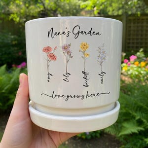 May include: A white ceramic mug with a black handle and the text "But First, Coffee" in a bold, black font. The mug is set against a blurred background, suggesting a cozy setting. The mug appears to be approximately 4 inches tall.