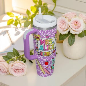Peut inclure: Un gobelet isotherme en acier inoxydable avec un couvercle blanc et une poign&eacute;e violette. Le gobelet pr&eacute;sente un motif de papier de cahier violet et blanc avec les mots "MRS. ALICE TEACH" en lettres color&eacute;es. Il a aussi une paille blanche.