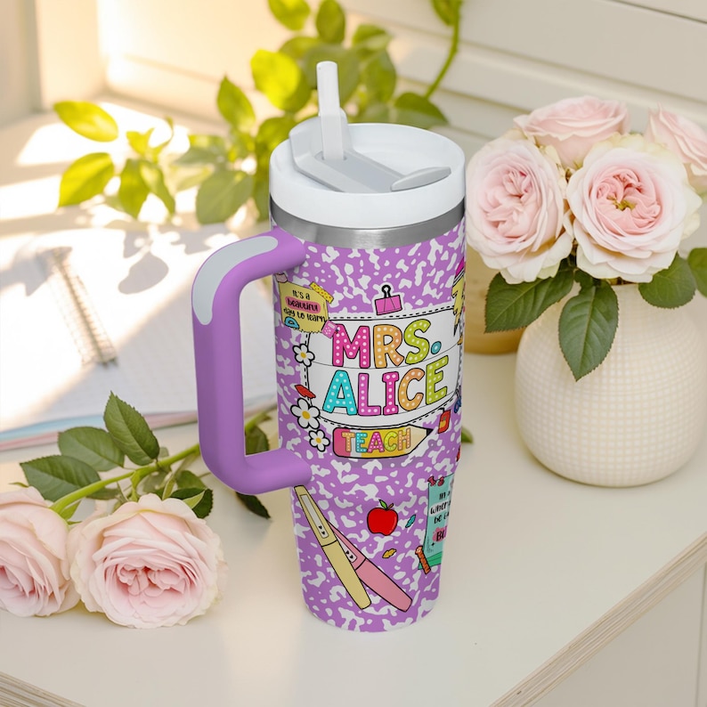 Peut inclure: Un gobelet isotherme en acier inoxydable avec un couvercle blanc et une poign&eacute;e violette. Le gobelet pr&eacute;sente un motif de papier de cahier violet et blanc avec les mots "MRS. ALICE TEACH" en lettres color&eacute;es. Il a aussi une paille blanche.