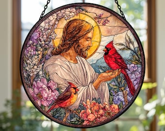 May include: Round stained glass window art featuring a religious figure with a halo, surrounded by flowers and two red cardinal birds. The artwork has a black metal frame and is suspended by a chain.