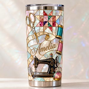 May include: A stainless steel tumbler featuring a stained glass pattern with sewing motifs including gold scissors, a measuring tape, spools of thread, a thimble, a pincushion, and a black sewing machine. The name Amelia is printed in script.