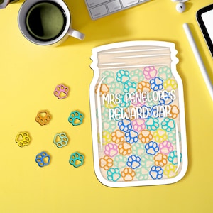 May include: A wooden cutout of a mason jar with a white rim and a white background. The jar is filled with colourful paw prints and the text "Mrs. Penelope's Reward Jar" is written on the jar.