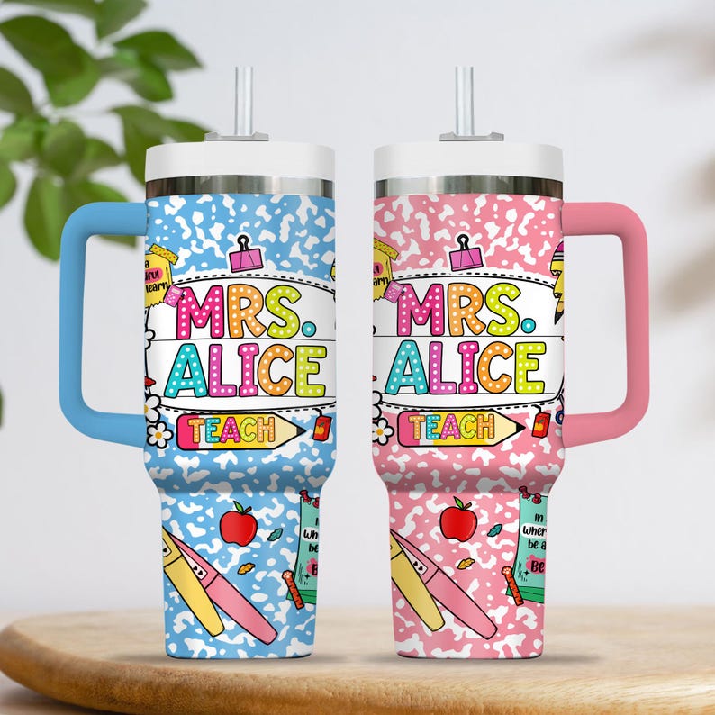 Peut inclure: Deux gobelets isothermes avec poign&eacute;es, un bleu et un rose, affichent le nom "MRS. ALICE" en lettres color&eacute;es. Les gobelets ont un couvercle blanc et une paille. Le design comprend des graphiques sur le th&egrave;me de l'&eacute;cole comme des pommes, des crayons et le mot "TEACH".