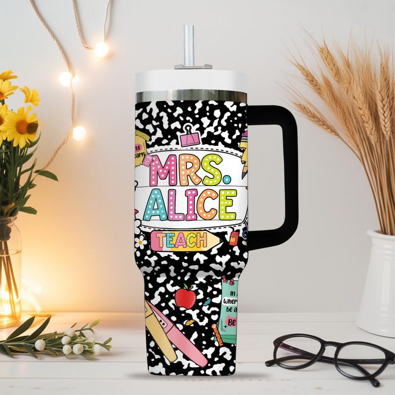 Peut inclure: Un grand gobelet isotherme avec une poign&eacute;e noire et un couvercle blanc. Le gobelet pr&eacute;sente un motif de cahier de composition noir et blanc avec le texte "MRS. ALICE TEACH" en lettres color&eacute;es. Le design comprend des illustrations sur le th&egrave;me de l'&eacute;cole.