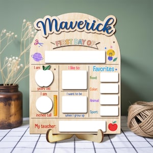 May include: Wooden first day of school sign with the name "Maverick" in blue script. The sign includes sections for age, height in inches, and favorite things. Decorative elements include an apple, a lightbulb, and a red apple.