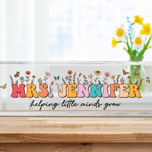 Può includere: Un blocco di acrilico trasparente con un design floreale colorato e il testo "MRS. JENNIFER helping little minds grow".