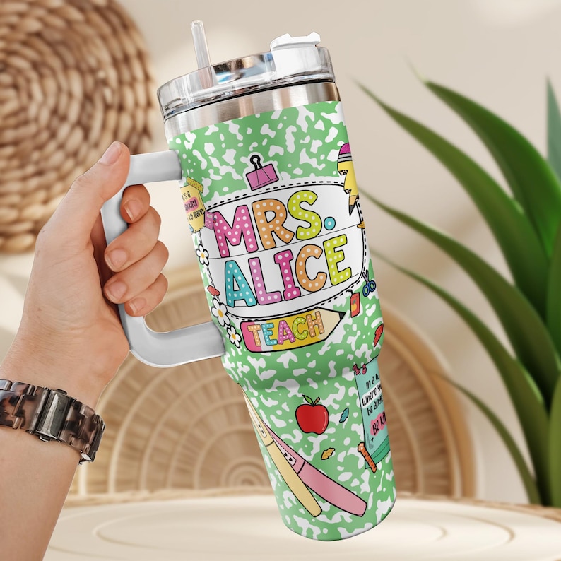 Peut inclure: Un gobelet en acier inoxydable avec une poign&eacute;e blanche et un couvercle transparent. Le gobelet est d&eacute;cor&eacute; d'un motif de papier de cahier vert et des mots "MRS. ALICE TEACH" en lettres color&eacute;es. Le gobelet pr&eacute;sente &eacute;galement des illustrations sur le th&egrave;me de l'&eacute;cole.